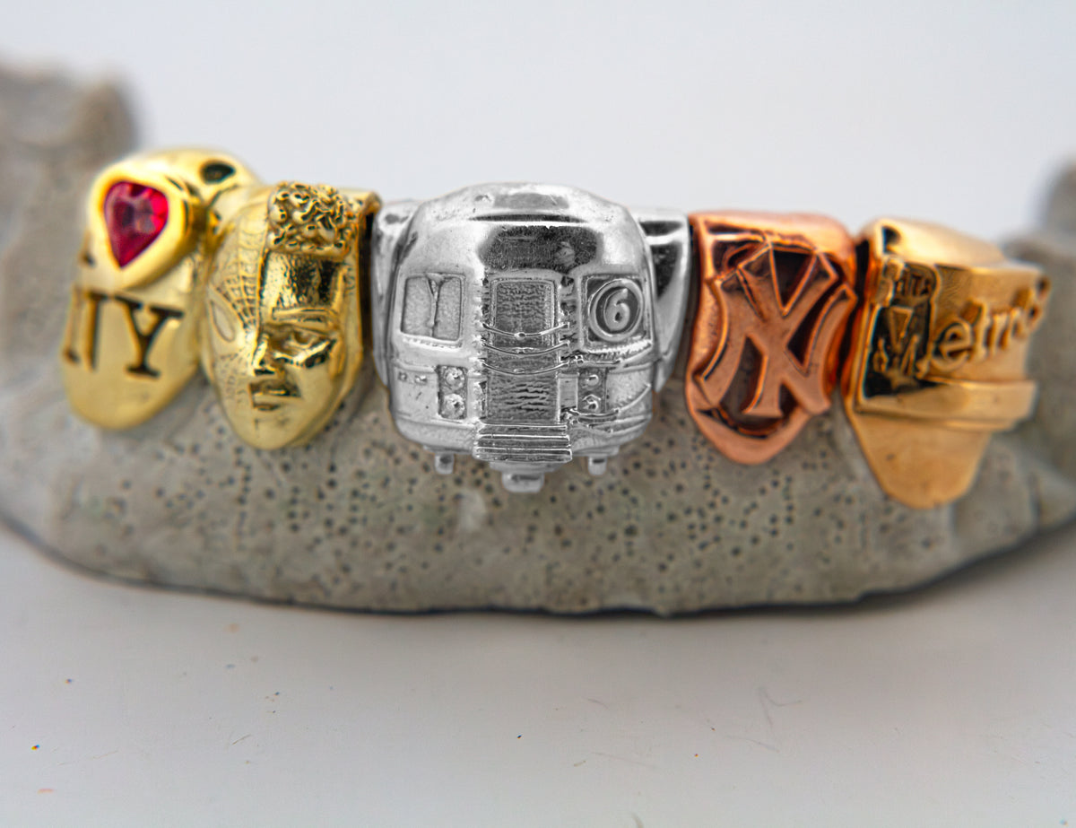 green gold with spiderman and I love new york logo with a garnet bezel set stone, yellow gold metro card rose gold yankees  and platinum 6 train grillz
